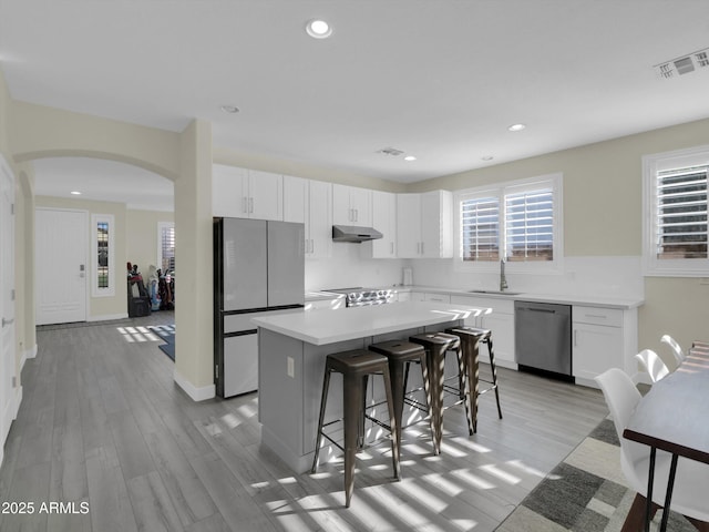 kitchen with stainless steel appliances, visible vents, a sink, a kitchen island, and under cabinet range hood