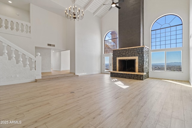 unfurnished living room with high vaulted ceiling, a stone fireplace, a wealth of natural light, and light hardwood / wood-style floors