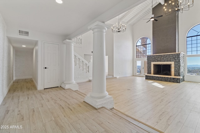 unfurnished living room with a stone fireplace, decorative columns, light hardwood / wood-style flooring, beam ceiling, and ceiling fan with notable chandelier