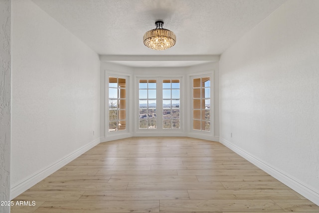 empty room featuring a textured ceiling, light hardwood / wood-style flooring, and a chandelier