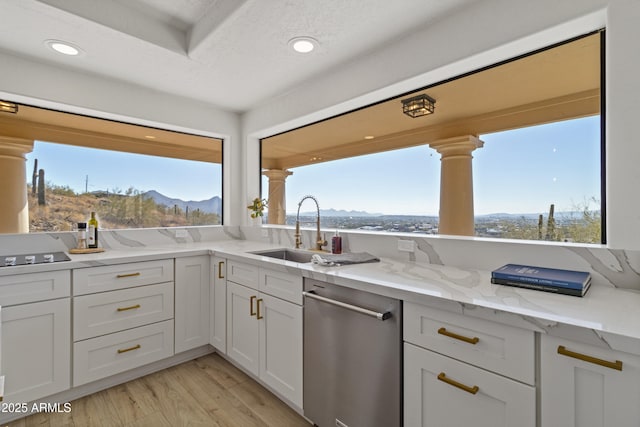 kitchen with white cabinetry, sink, stainless steel dishwasher, a mountain view, and light stone countertops