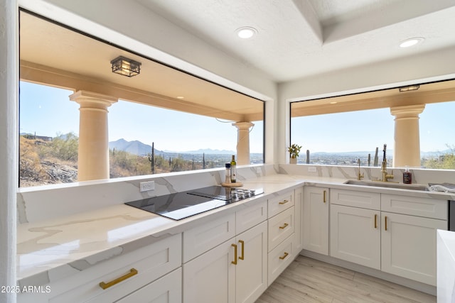 kitchen featuring plenty of natural light, a mountain view, black electric stovetop, light stone countertops, and white cabinets