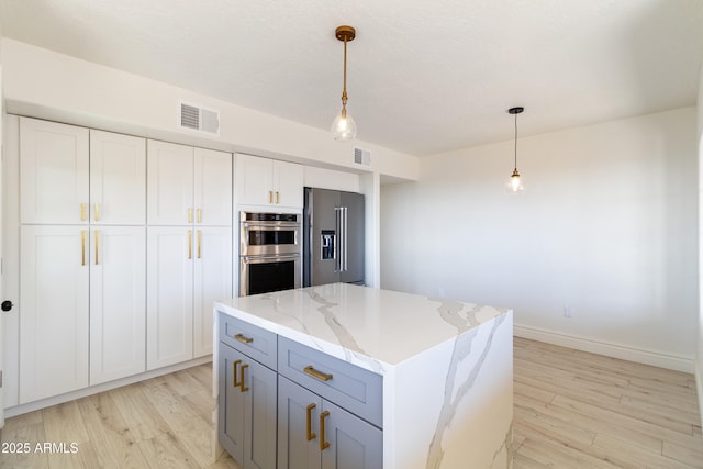 kitchen with a kitchen island, appliances with stainless steel finishes, decorative light fixtures, white cabinetry, and light stone countertops