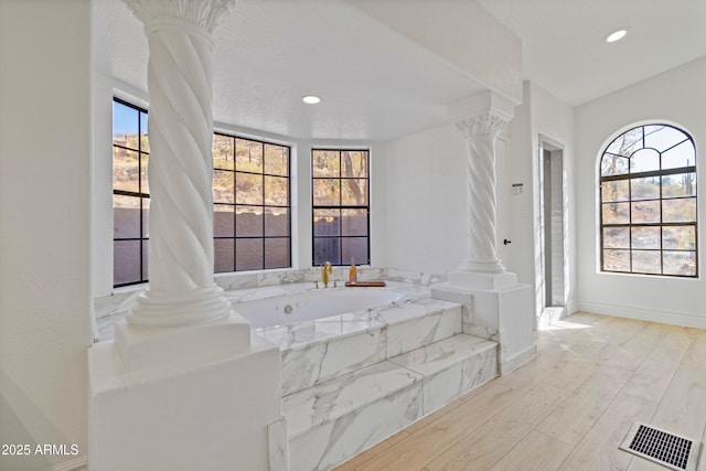 bathroom featuring a relaxing tiled tub, wood-type flooring, and ornate columns