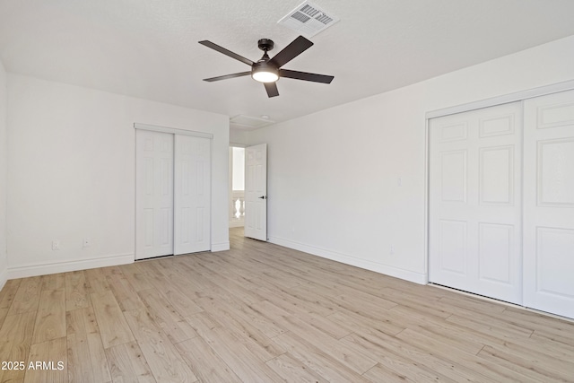 unfurnished bedroom featuring ceiling fan, multiple closets, and light wood-type flooring