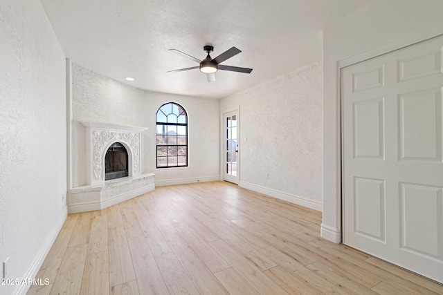 unfurnished living room featuring ceiling fan, a fireplace, light hardwood / wood-style floors, and a textured ceiling