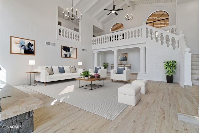 living room featuring decorative columns, high vaulted ceiling, light wood-type flooring, beam ceiling, and ceiling fan with notable chandelier