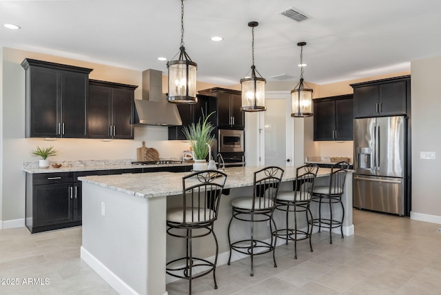 kitchen featuring island range hood, a center island with sink, stainless steel appliances, hanging light fixtures, and light stone counters