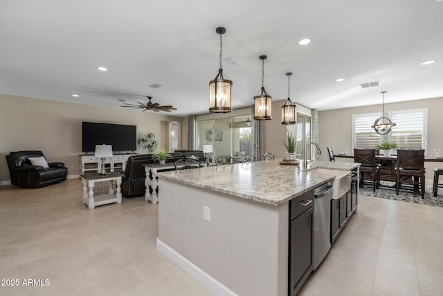 kitchen featuring a center island with sink, hanging light fixtures, light stone countertops, ceiling fan, and sink