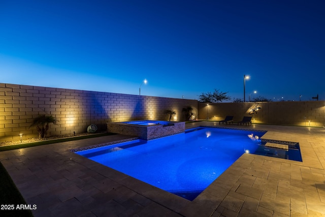 pool at dusk featuring a patio, pool water feature, and an in ground hot tub