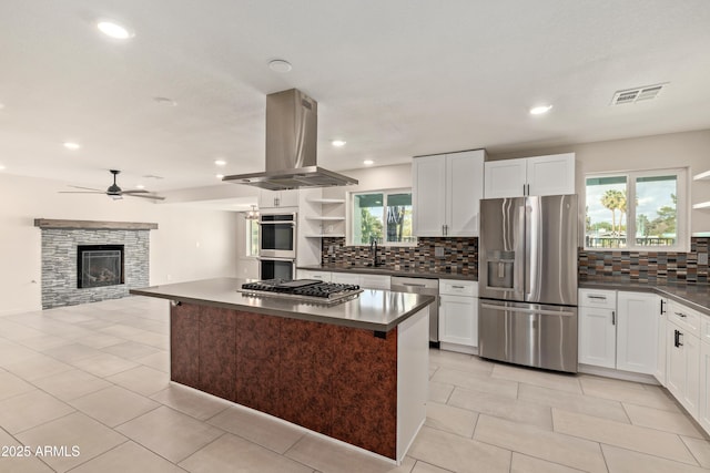 kitchen featuring open shelves, stainless steel appliances, dark countertops, visible vents, and island range hood