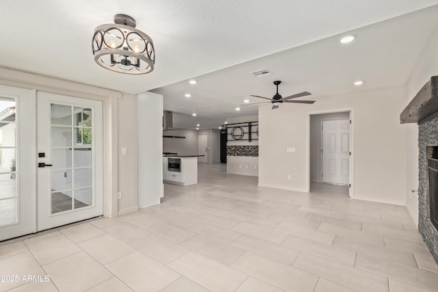 unfurnished living room with recessed lighting, ceiling fan with notable chandelier, visible vents, and a stone fireplace