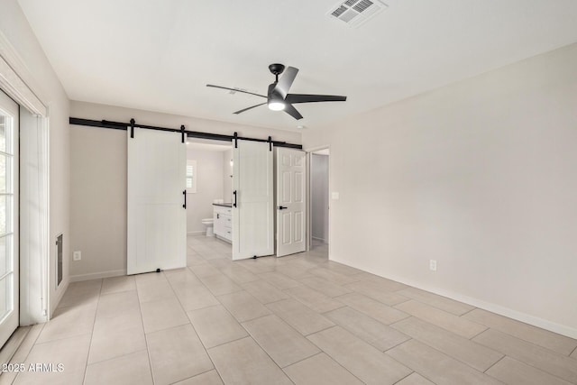 empty room featuring ceiling fan, a barn door, visible vents, and baseboards