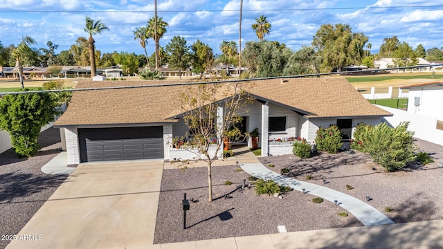 mid-century home featuring driveway, a shingled roof, a garage, and brick siding