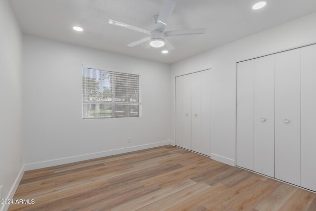 unfurnished bedroom featuring ceiling fan, light hardwood / wood-style floors, and two closets