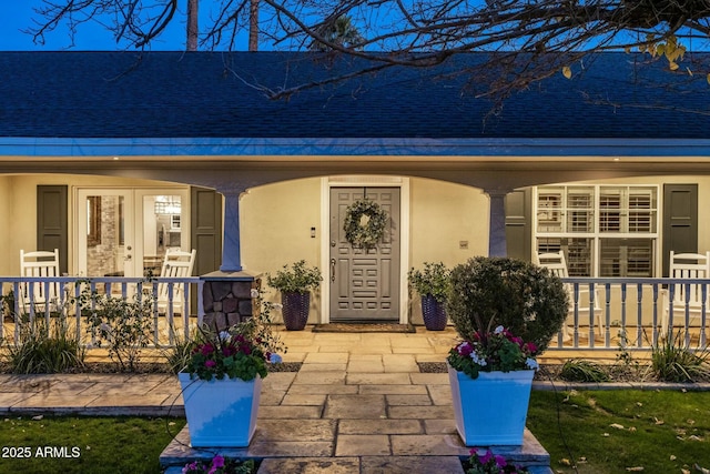 view of exterior entry featuring a shingled roof, a porch, and stucco siding