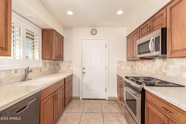 kitchen featuring backsplash, sink, light stone countertops, light tile patterned floors, and stainless steel appliances