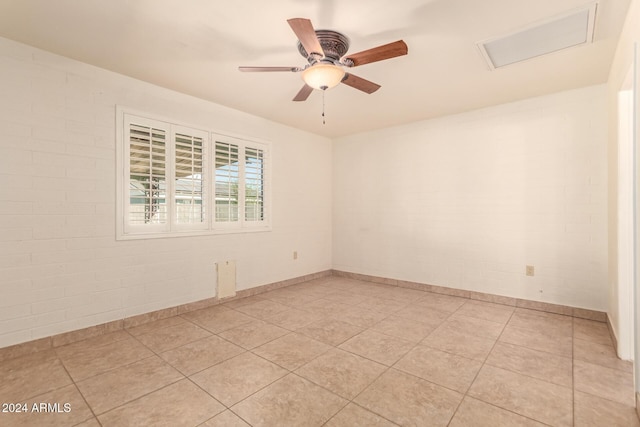 tiled spare room with ceiling fan and brick wall