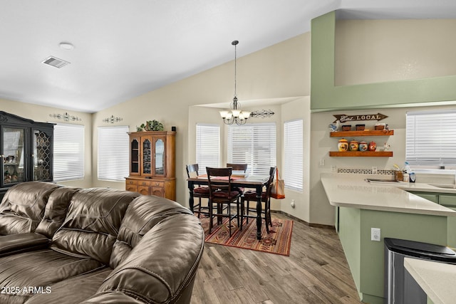 living room featuring an inviting chandelier, light hardwood / wood-style flooring, plenty of natural light, and vaulted ceiling