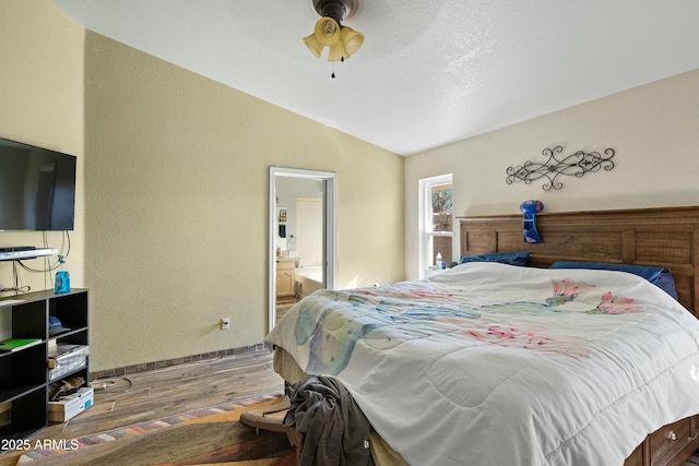 bedroom featuring ceiling fan, ensuite bath, lofted ceiling, and hardwood / wood-style floors