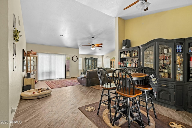 dining space featuring lofted ceiling, bar area, a textured ceiling, ceiling fan, and light hardwood / wood-style floors