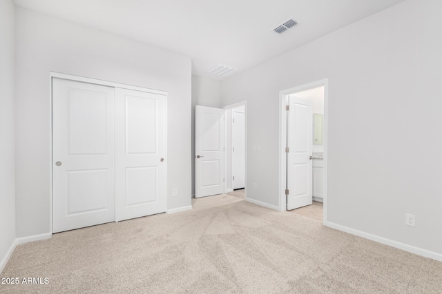 unfurnished bedroom with ensuite bathroom, light colored carpet, and a closet