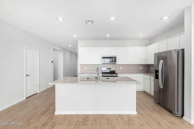 kitchen featuring a kitchen island with sink, white cabinets, sink, light stone countertops, and appliances with stainless steel finishes