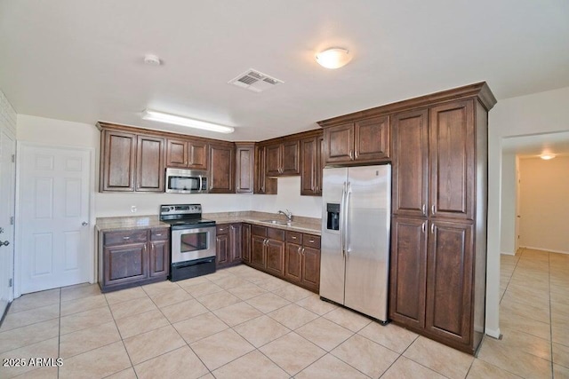 kitchen featuring stainless steel appliances, light tile patterned floors, dark brown cabinets, and sink