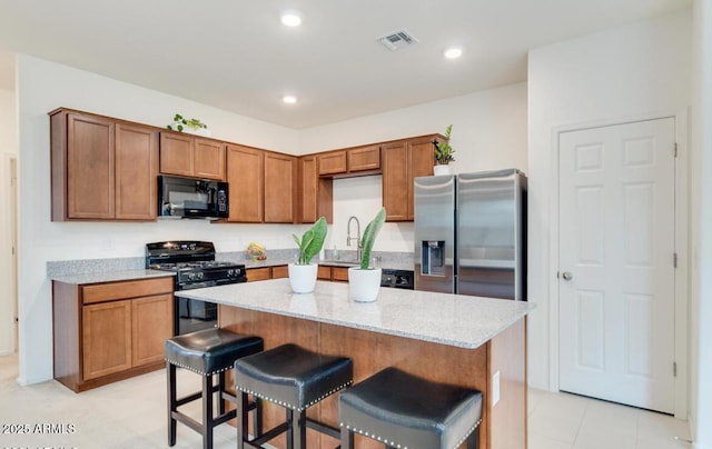 kitchen featuring visible vents, black appliances, light stone counters, a kitchen breakfast bar, and a center island