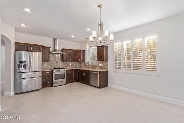 kitchen featuring pendant lighting, decorative backsplash, stainless steel appliances, dark brown cabinets, and wall chimney range hood