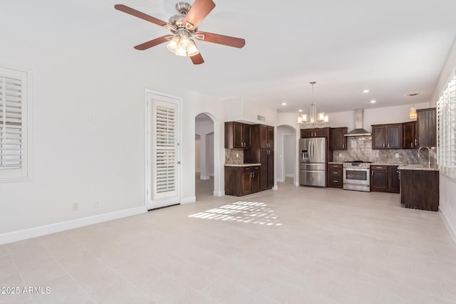 kitchen featuring pendant lighting, dark brown cabinets, stainless steel appliances, decorative backsplash, and wall chimney exhaust hood