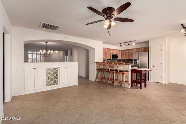 kitchen featuring hanging light fixtures, appliances with stainless steel finishes, backsplash, light tile patterned floors, and a breakfast bar