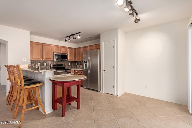 kitchen with appliances with stainless steel finishes, decorative backsplash, kitchen peninsula, light tile patterned floors, and a breakfast bar area