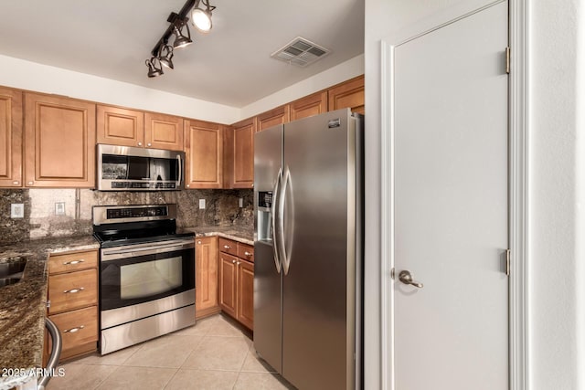 kitchen with dark stone countertops, appliances with stainless steel finishes, decorative backsplash, and light tile patterned flooring