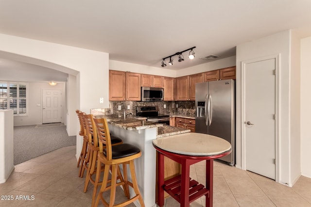 kitchen featuring decorative backsplash, light colored carpet, kitchen peninsula, stainless steel appliances, and a breakfast bar area