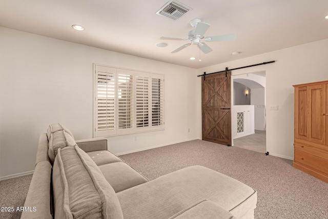 living area featuring light colored carpet, ceiling fan, and a barn door