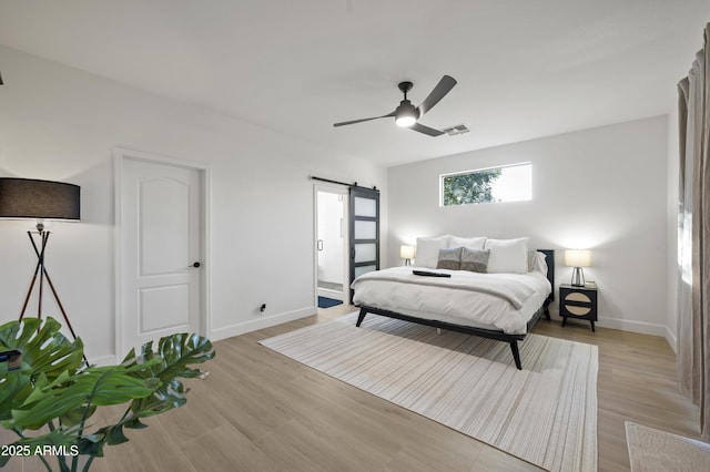 bedroom with a barn door, baseboards, light wood-style floors, and visible vents