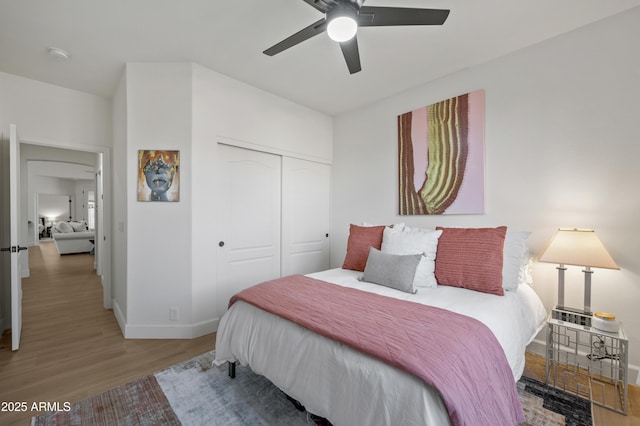 bedroom with a closet, baseboards, wood finished floors, and a ceiling fan