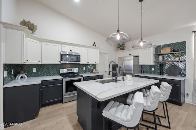 kitchen featuring an island with sink, a sink, open shelves, white cabinetry, and appliances with stainless steel finishes