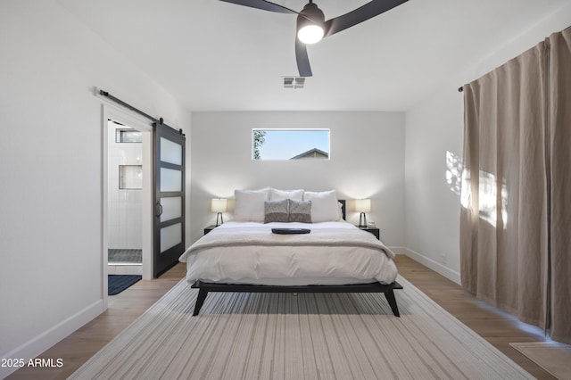 bedroom featuring light wood finished floors, visible vents, baseboards, and a barn door