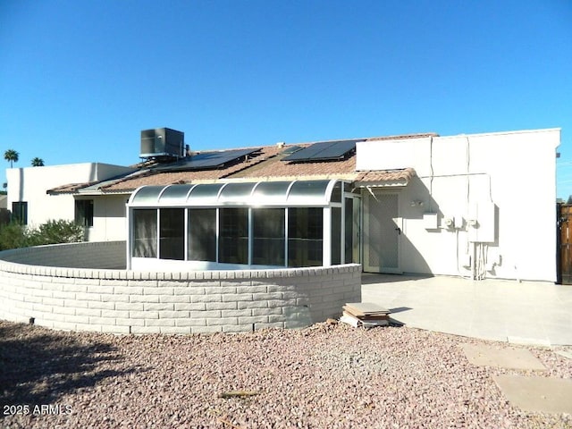 rear view of house with roof mounted solar panels, a sunroom, central AC, and a patio
