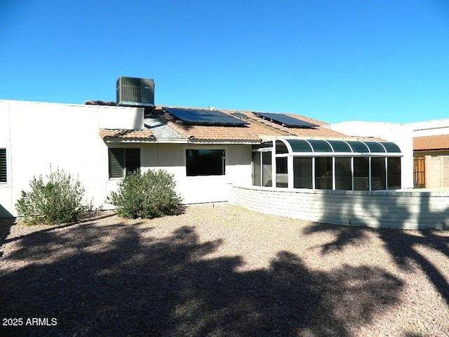 back of house with stucco siding, solar panels, a sunroom, and central AC unit