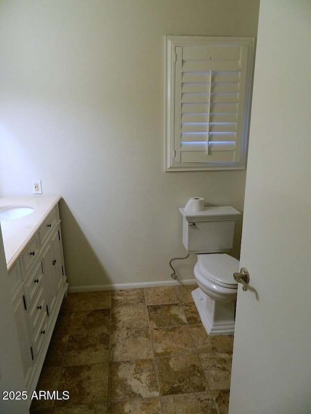 bathroom with baseboards, toilet, vanity, and stone finish floor