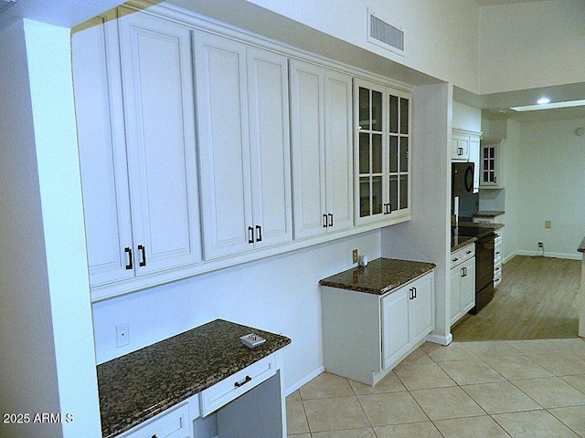 kitchen with dark stone countertops, black appliances, light tile patterned flooring, glass insert cabinets, and visible vents
