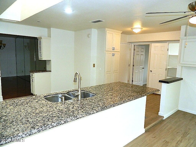 kitchen with a ceiling fan, wood finished floors, a sink, white cabinets, and visible vents