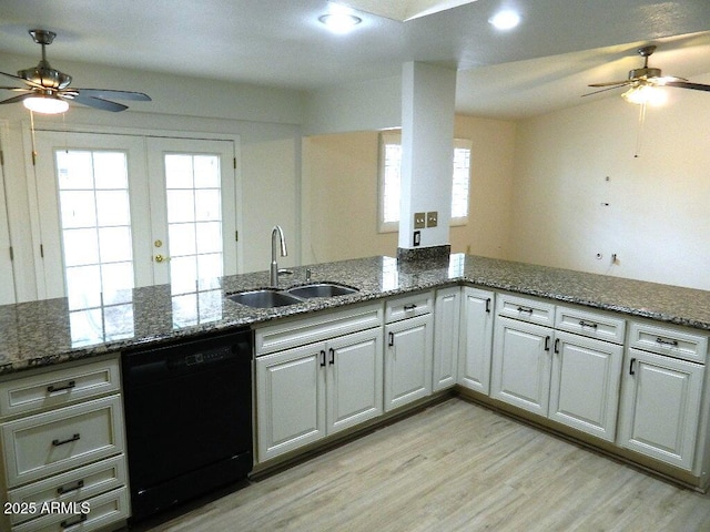kitchen with light wood finished floors, a sink, a peninsula, black dishwasher, and ceiling fan