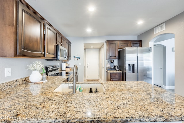 kitchen with light stone countertops, dark brown cabinetry, stainless steel appliances, and sink