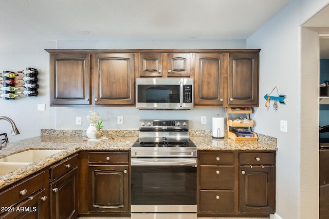 kitchen with light stone countertops, sink, dark brown cabinets, and appliances with stainless steel finishes