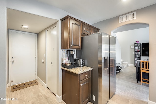 kitchen with stainless steel fridge, dark brown cabinets, light stone counters, and light wood-type flooring