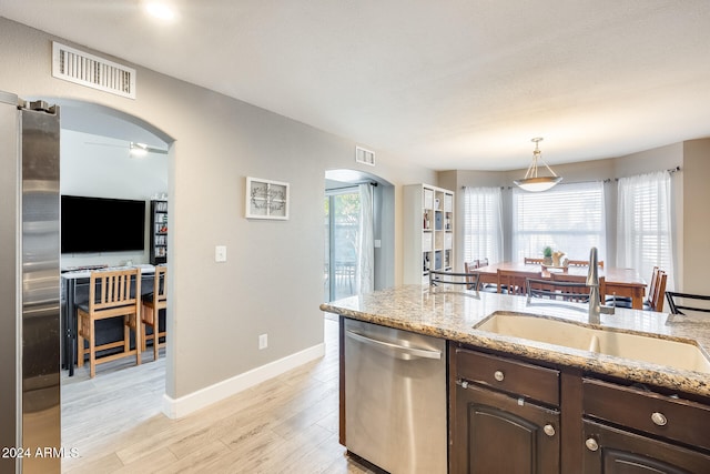 kitchen with appliances with stainless steel finishes, a wealth of natural light, dark brown cabinetry, sink, and light hardwood / wood-style floors